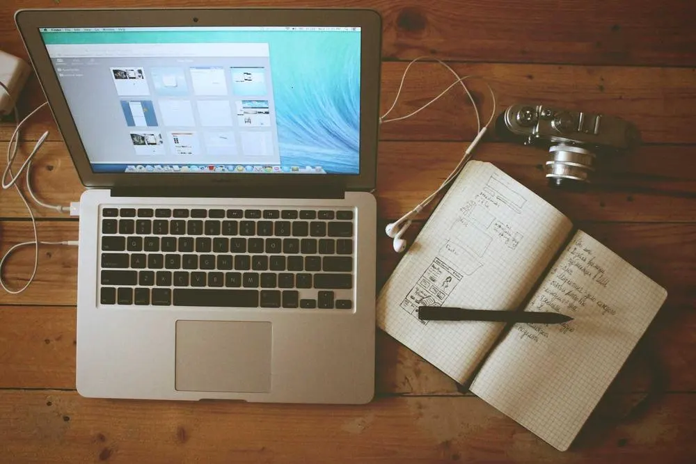 Laptop mit geöffneter Anwendung neben einem Notizbuch mit Skizzen