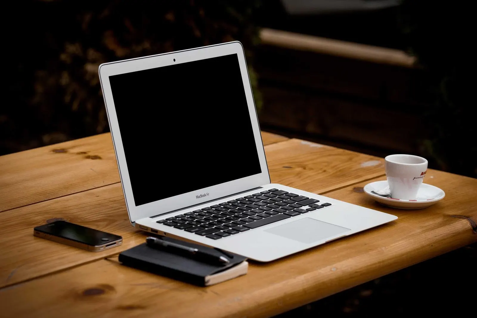 Aufgeklappter Laptop mit Notizbuch und Kaffee auf einem Holztisch